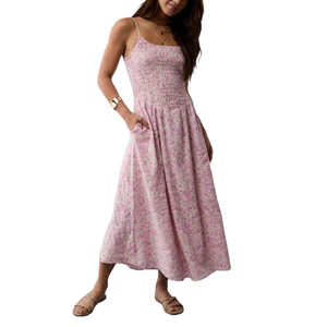 Pink floral midi dress with a smocked bodice, spaghetti straps, and flowing silhouette, featuring pockets. Paired with flat braided sandals and a gold bracelet.
