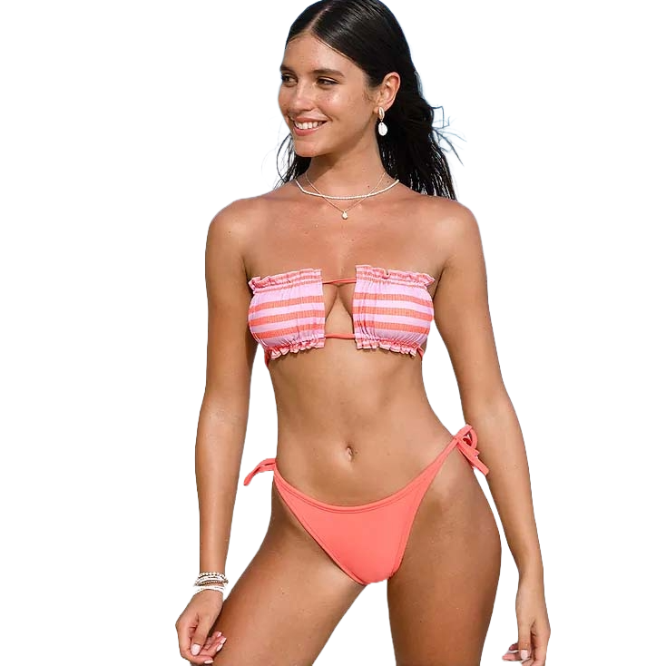 A woman is wearing a pink and white striped bandeau bikini top with ruffle details and matching solid pink, tie-side bikini bottoms.