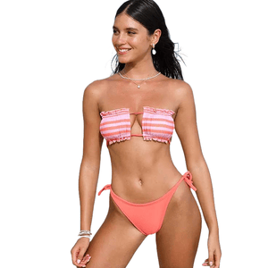 A woman is wearing a pink and white striped bandeau bikini top with ruffle details and matching solid pink, tie-side bikini bottoms.