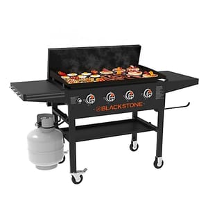 A Blackstone outdoor griddle grill with four burners, featuring a flat top cooking surface, side shelves, and a propane tank underneath.