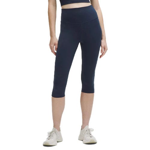 A person wearing high-waisted navy capri leggings and white sneakers, paired with a cropped black top.