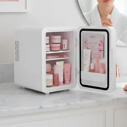 A small fridge with various pink skincare products is open on a marble countertop in a bathroom, accompanied by a woman applying a product.