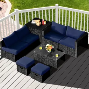 Outdoor patio set with dark wicker furniture, blue cushions, and a glass-top coffee table. Includes an L-shaped sofa, two stools, and a multi-level corner piece with snacks and drinks displayed.