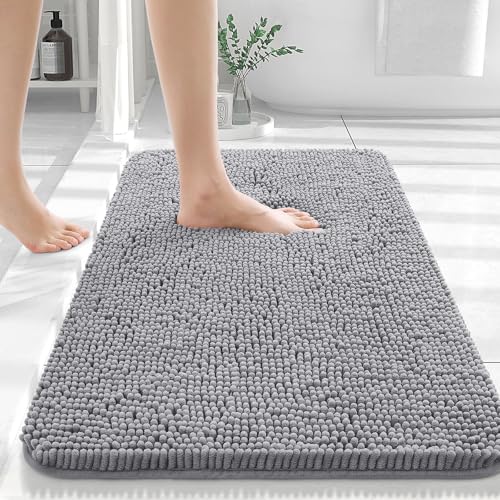 A gray chenille bath rug is displayed, featuring a thick, plush texture with an individual stepping onto it with bare feet.