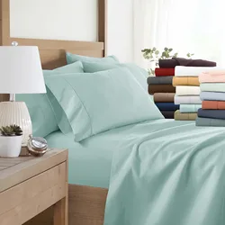 A neatly made bed with light blue sheets and pillowcases is shown, alongside a stack of additional bed linens in various colors. A small bedside table with a lamp and decorative items is visible.