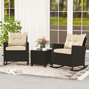 A patio set with two wicker rocking chairs featuring beige cushions and a matching side table. A decorative rug, potted plant, and a vase with flowers complement the setup.