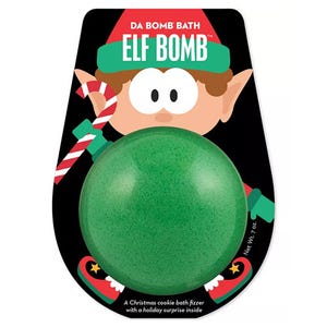 Da Bomb Elf Bath Bomb is a green bath fizzer with a Christmas cookie scent, featuring a holiday surprise inside. The packaging includes an illustration of an elf holding a candy cane.