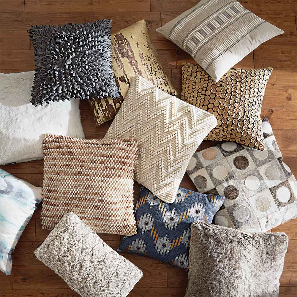 A variety of decorative throw pillows with different textures and patterns are scattered on a wooden floor.
