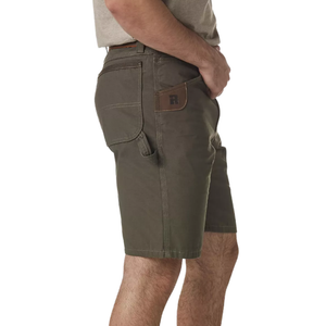 A person wearing dark green work shorts with a side utility pocket and belt loops, featuring reinforced stitching and a patch detail on the pocket.