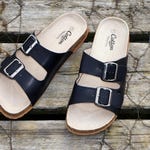 A pair of black two-strap sandals with buckle closures and beige footbeds, displayed on a wooden surface.