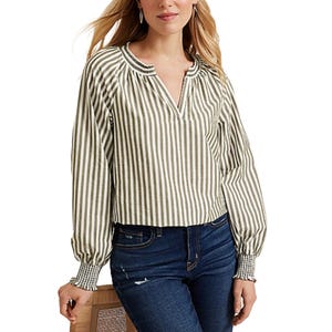 A woman wears a long-sleeve, striped blouse with a split neckline and smocked cuffs, paired with dark blue jeans.