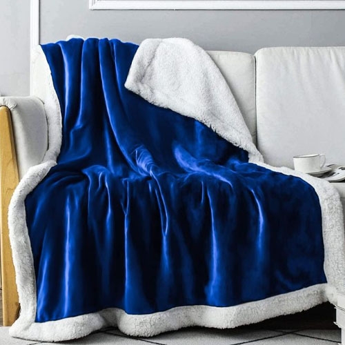 A blue, plush throw blanket with a white fluffy underside is draped over a white sofa.