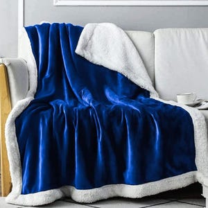 A blue, plush throw blanket with a white fluffy underside is draped over a white sofa.