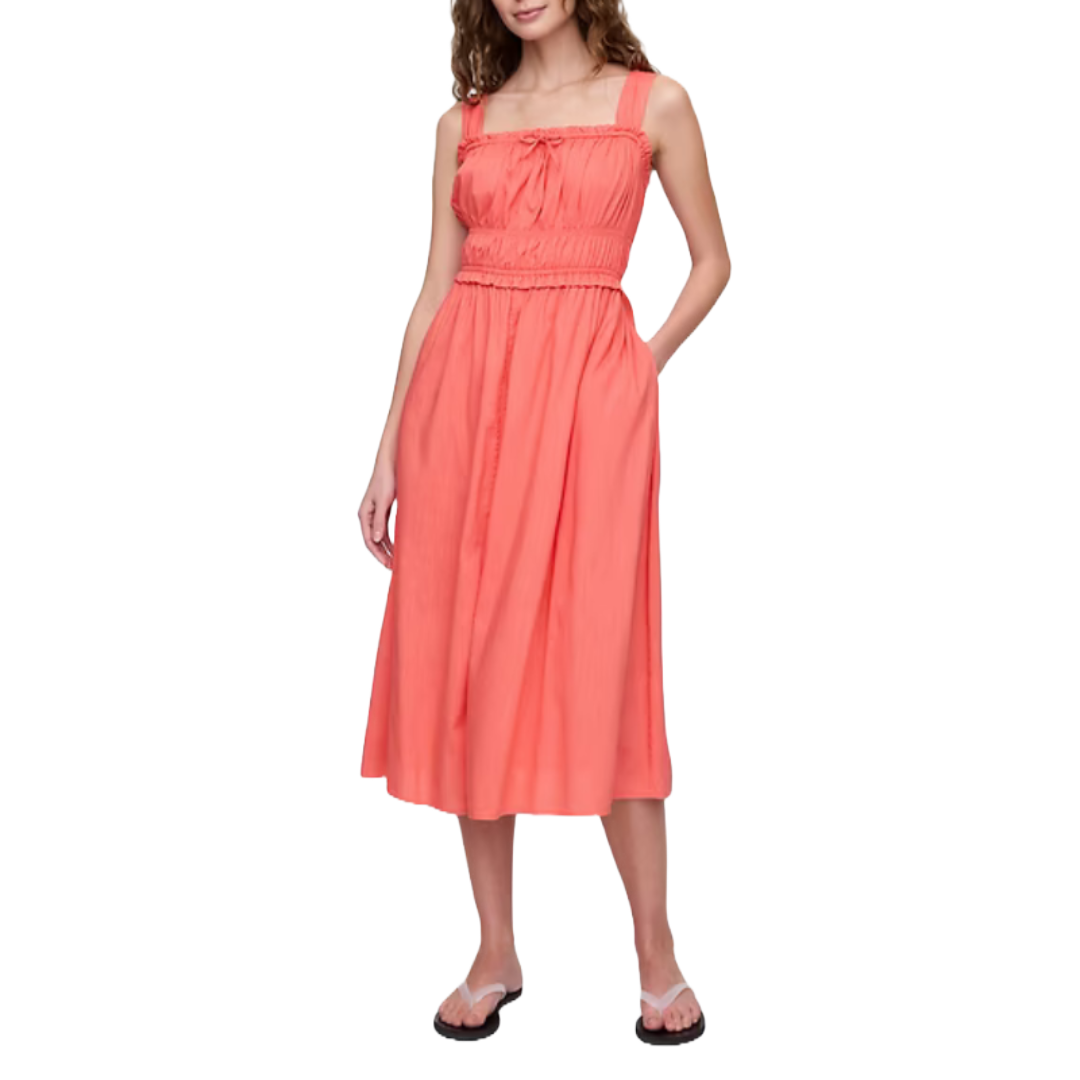 Coral smocked midi dress featuring wide shoulder straps, a cinched waist, and flowing skirt. Paired with flip-flops, offering a casual yet stylish look.