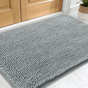 A gray chenille rug with a textured, looped surface is placed in front of a wooden door, accompanied by a potted plant on the side.
