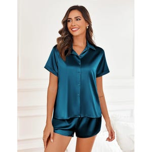 A woman is wearing a teal satin pajama set with a short-sleeved button-up shirt and matching shorts.
