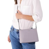 A person is wearing a white blouse and blue jeans, holding a light purple crossbody bag with a thin strap.