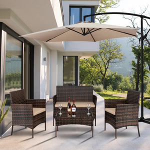 4-piece patio set includes a two-seater sofa, two armchairs, and a glass-top coffee table, all in brown wicker with beige cushions. An umbrella provides shade, and wine bottles with glasses are set on the table.