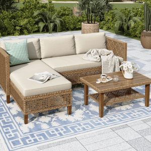 A wicker patio sofa set featuring beige cushions with one teal pillow and a knitted throw, paired with a matching wooden coffee table. The setup includes a blue and white patterned outdoor rug and a white flower vase on the table.