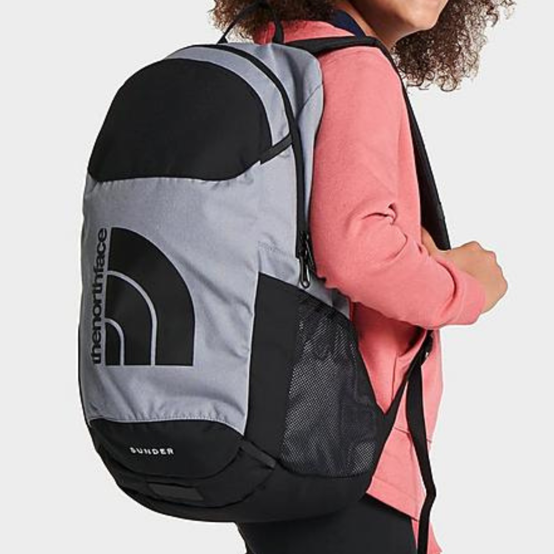 A person wearing a grey and black backpack with a logo on it.