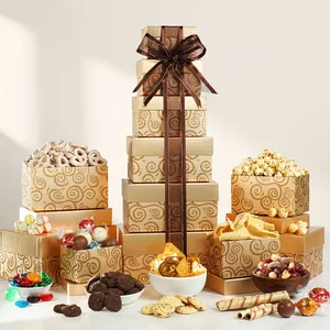 A stack of gift boxes with swirling patterns and a brown ribbon contains assorted treats like pretzels, popcorn, cookies, candies, and wafers, displayed alongside.