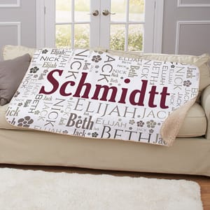 A personalized blanket featuring the name \“Schmidtt\“ prominently, surrounded by additional names like Elijah, Beth, Jack, and Nick, along with paw prints, displayed on a sofa.