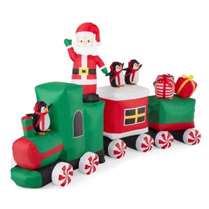 A large inflatable Christmas decoration in the shape of a train, featuring a waving Santa, two penguins, gifts, and candy cane details. Its festive colors are primarily red, green, and white.