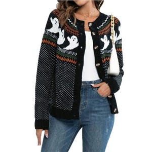 A black cardigan featuring a playful ghost pattern design, worn over a white top and paired with jeans.