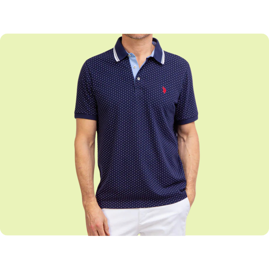 Navy blue polo shirt with white polka dots, featuring a contrasting collar and a red embroidered logo, paired with white shorts.