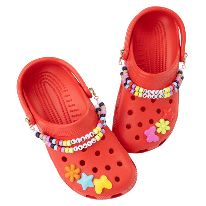 Pair of red clogs decorated with colorful charms and beads, featuring text like \“EXTRA VIBES\“ and \“FEELS IYKYK.\“