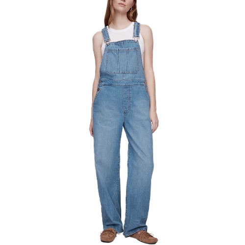 Women's relaxed fit denim overalls from Gap Factory feature adjustable shoulder straps, a chest pocket, side pockets, and a straight-leg design. Paired with a white tank top and brown shoes.