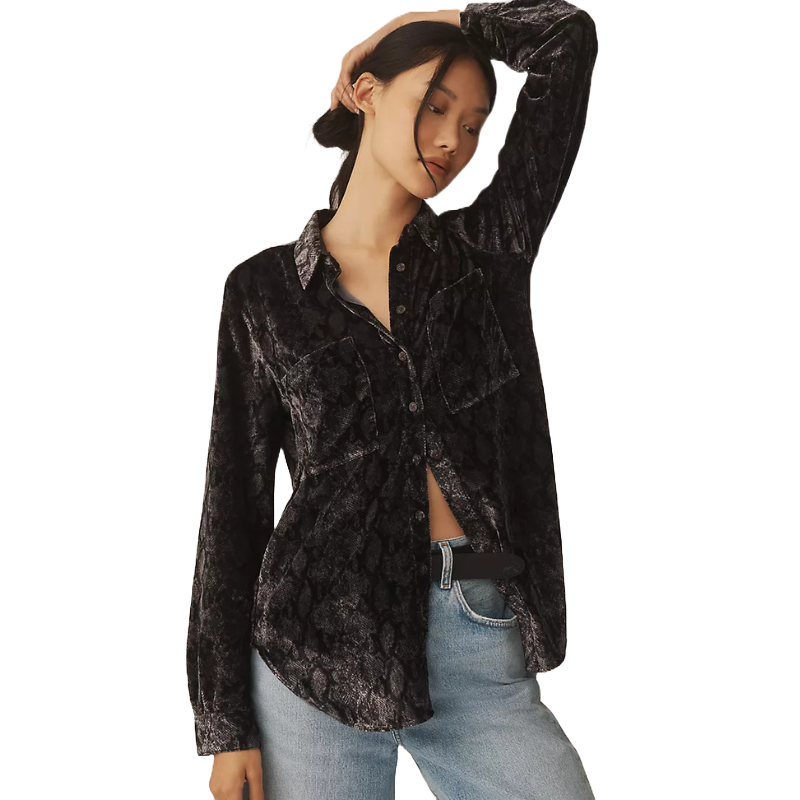 A woman wearing a black, textured button-down shirt with a subtle pattern, featuring two front pockets. The shirt is paired with light blue jeans and a black belt.