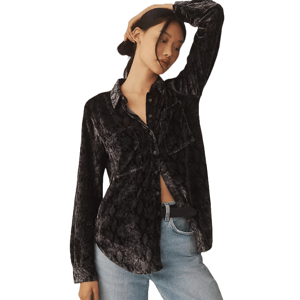 A woman wearing a black, textured button-down shirt with a subtle pattern, featuring two front pockets. The shirt is paired with light blue jeans and a black belt.