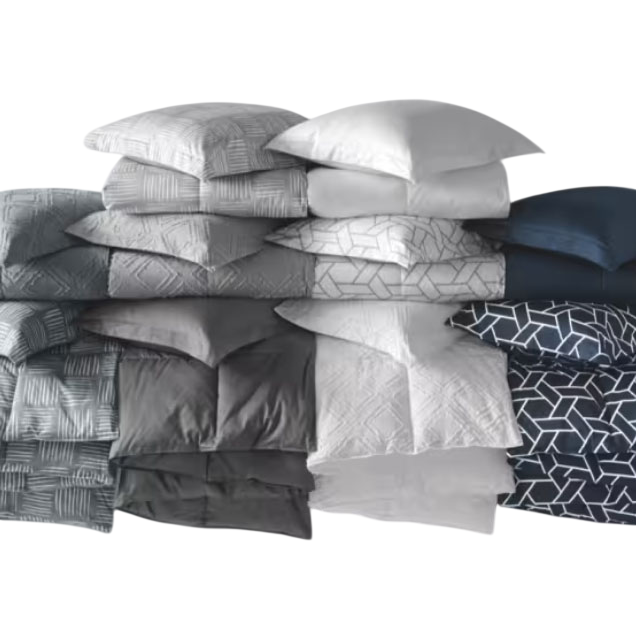 A stack of pillows and matching bedding in various shades of gray, blue, and white with geometric patterns.
