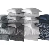 A stack of pillows and matching bedding in various shades of gray, blue, and white with geometric patterns.