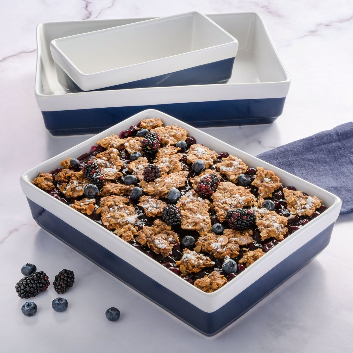 Set of blue and white ceramic baking dishes filled with a mixed berry crumble, featuring blackberries and blueberries.