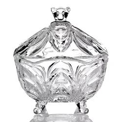 A decorative glass container with an ornate lid and elegant, sculpted design, supported by three small spherical feet.
