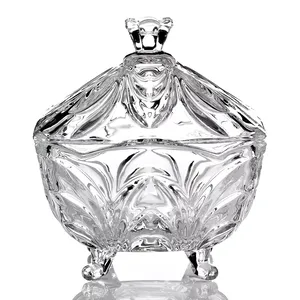 A decorative glass container with an ornate lid and elegant, sculpted design, supported by three small spherical feet.