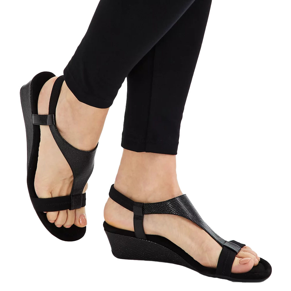 Black wedge sandals with a textured surface, featuring a T-strap design and ankle strap, worn with black leggings.