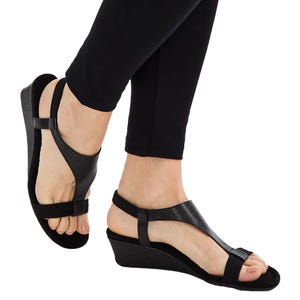 Black wedge sandals with a textured surface, featuring a T-strap design and ankle strap, worn with black leggings.