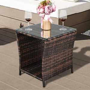 Square outdoor side table with a glass top and brown woven rattan body, featuring two wine glasses and a pink floral arrangement in a gold vase on top.