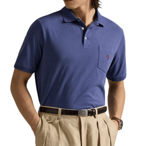A man wears a blue polo shirt with a pocket featuring a red logo, paired with beige pleated trousers and a black belt.