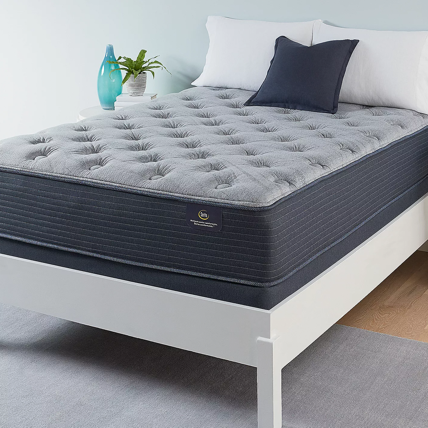 A mattress on a bed frame with white sheets, a navy blue pillow, and decorative items on a side table.