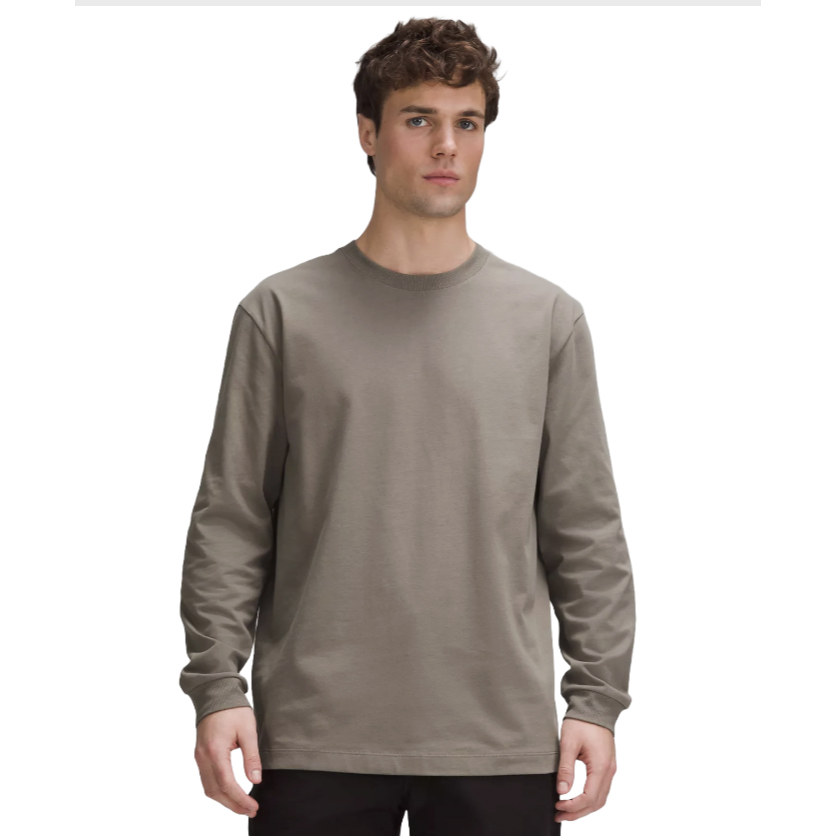 A man is wearing a long-sleeved, heavyweight tee in a solid khaki color with a crew neck and a regular fit.