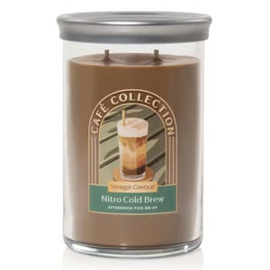 Yankee Candle's Café Collection features a \“Nitro Cold Brew\“ scented candle with two wicks, housed in a clear glass jar with a silver lid, featuring an illustration of a cold brew coffee on the label.