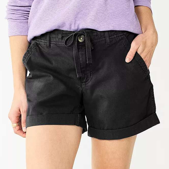 A person wearing black denim shorts with a drawstring waist.