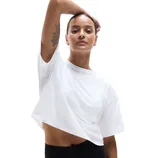 A person wearing a loose-fitting, white cropped T-shirt and black pants, lifting one arm.