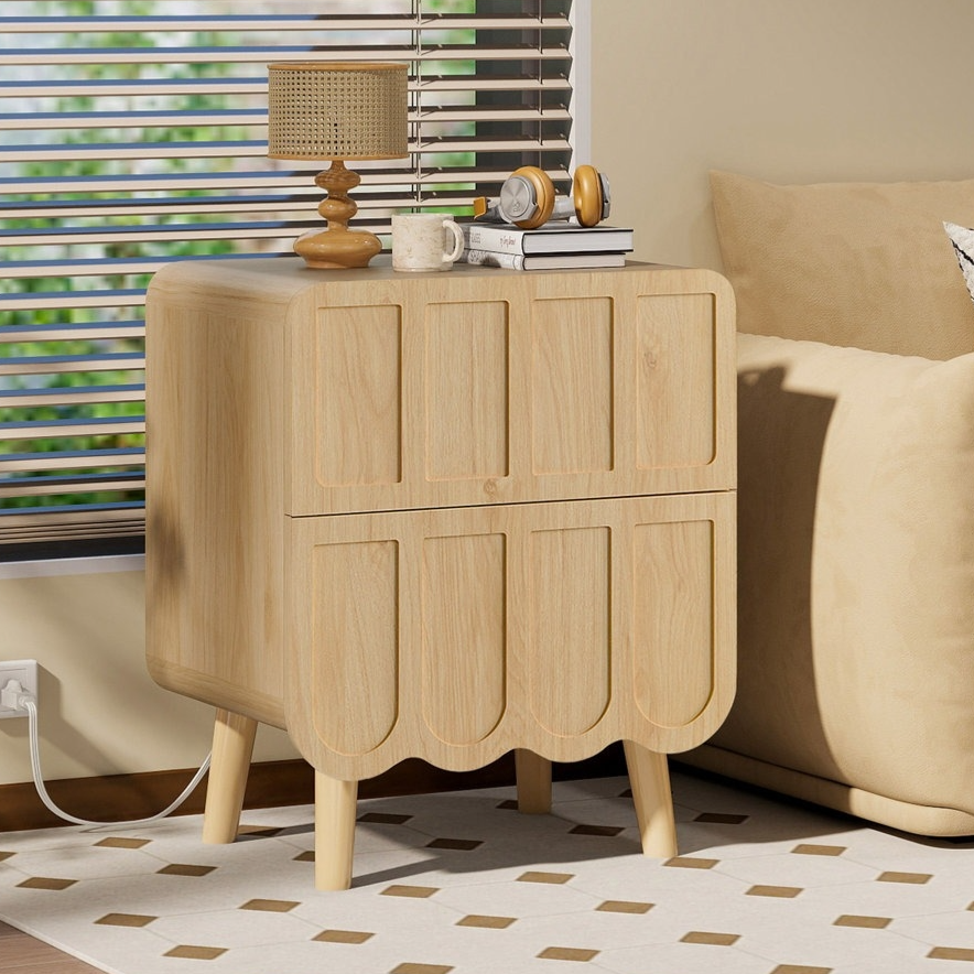 A wooden side table with a unique panel design stands beside a beige sofa, featuring a lamp, books, and a clock on top. A patterned cushion is on the sofa, and blinds cover the window behind them.