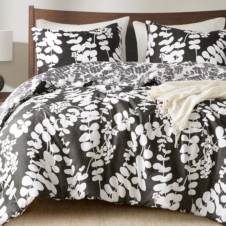 A bed is adorned with a black and white floral-patterned comforter and matching pillows, complemented by a light beige throw blanket on top.