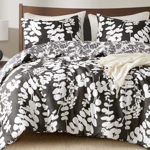 A bed is adorned with a black and white floral-patterned comforter and matching pillows, complemented by a light beige throw blanket on top.